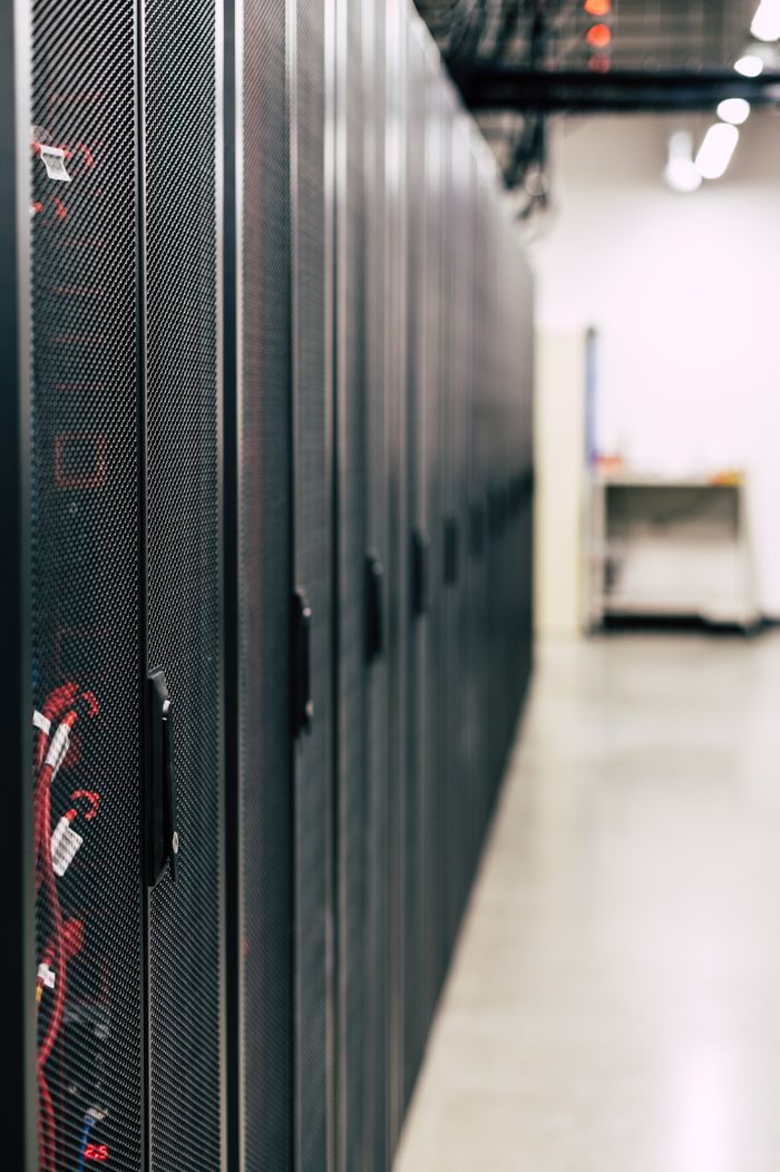 Metal black cabinets with servers inside with red wires connected standing in row in lighted room