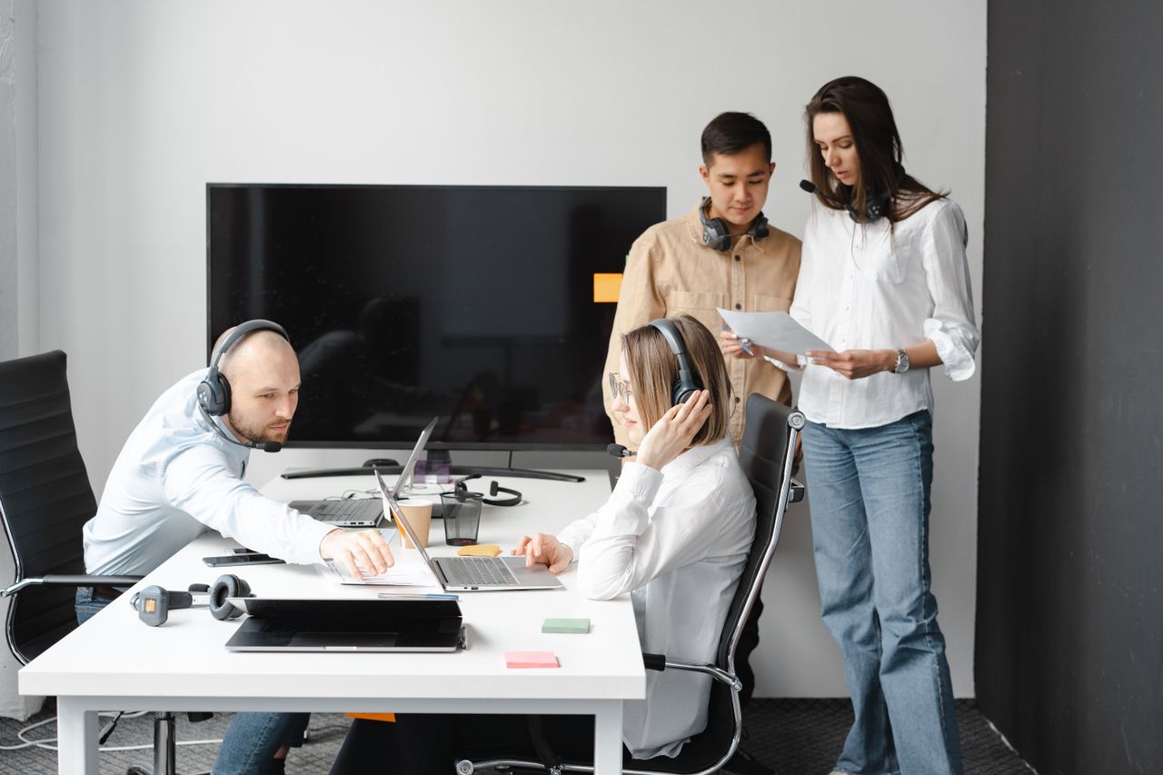 Group of diverse colleagues working together in a modern office environment with headsets and laptops.